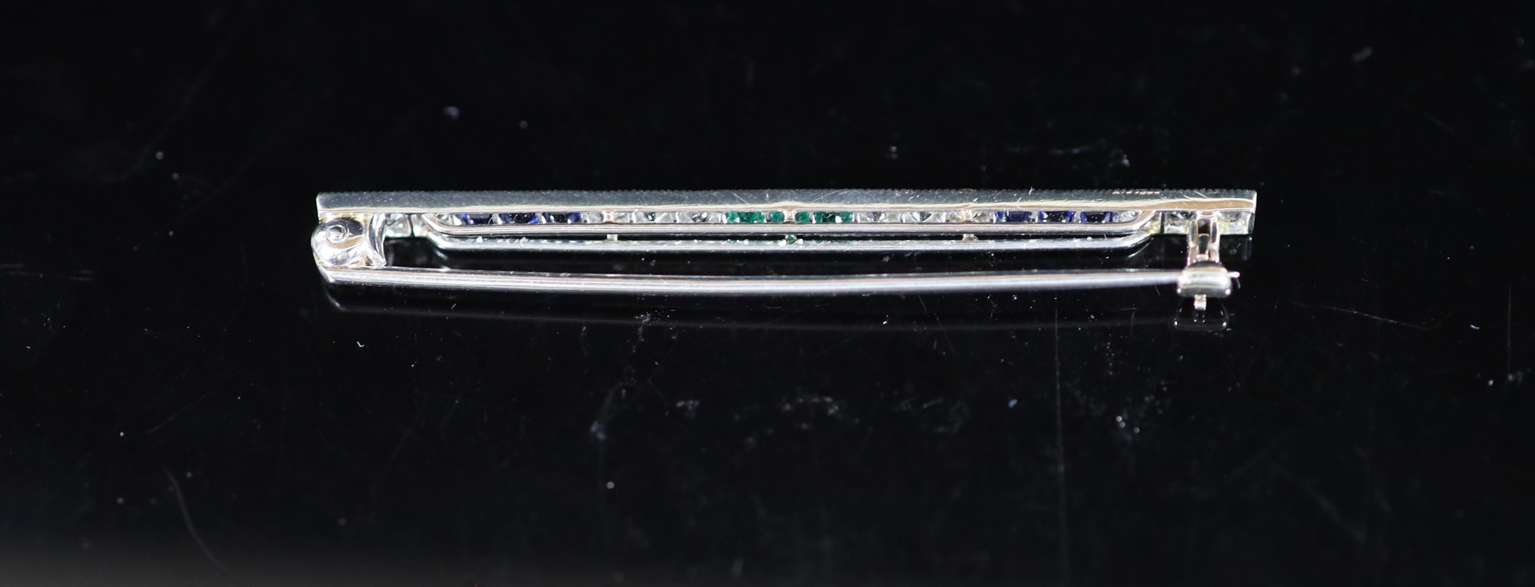 A mid 20th century Cartier platinum, twelve stone diamond, six stone sapphire and three stone emerald miilegrain set bar brooch